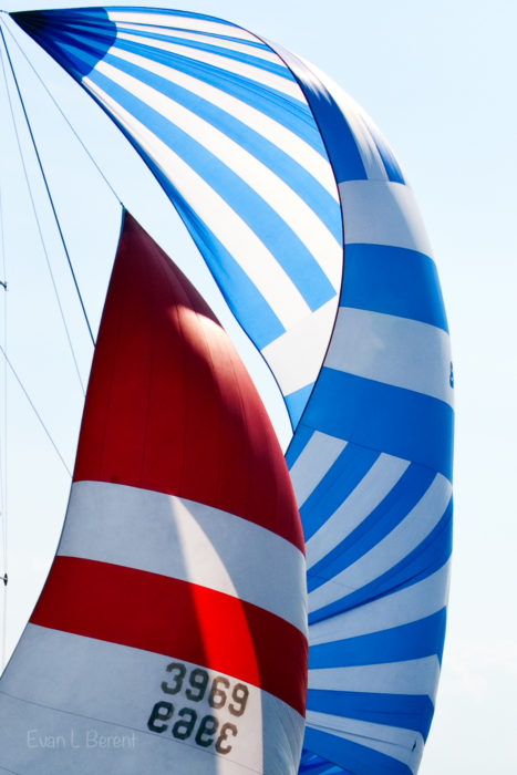 A red and white spinnaker is flanked by a larger blue and white spinnaker.