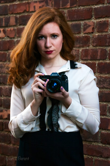 A woman holds a film camera up at you.