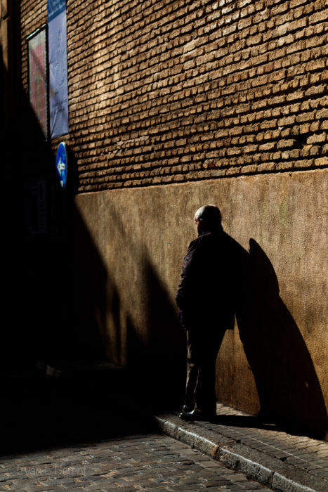 A man rests against a wall with long shadows.